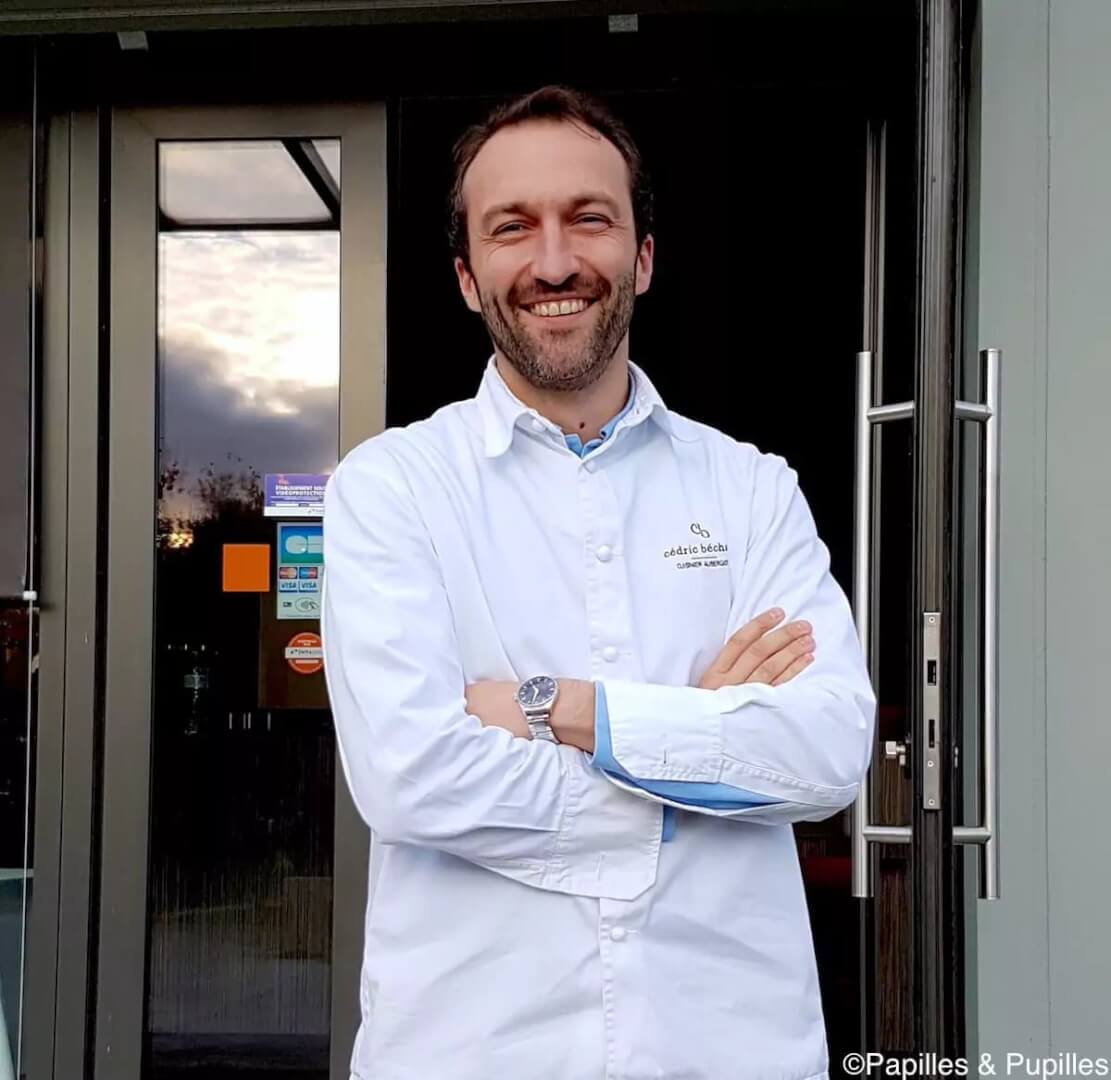 Homme souriant en chemise blanche devant une entrée, spécialiste en réservation pour le Gers.